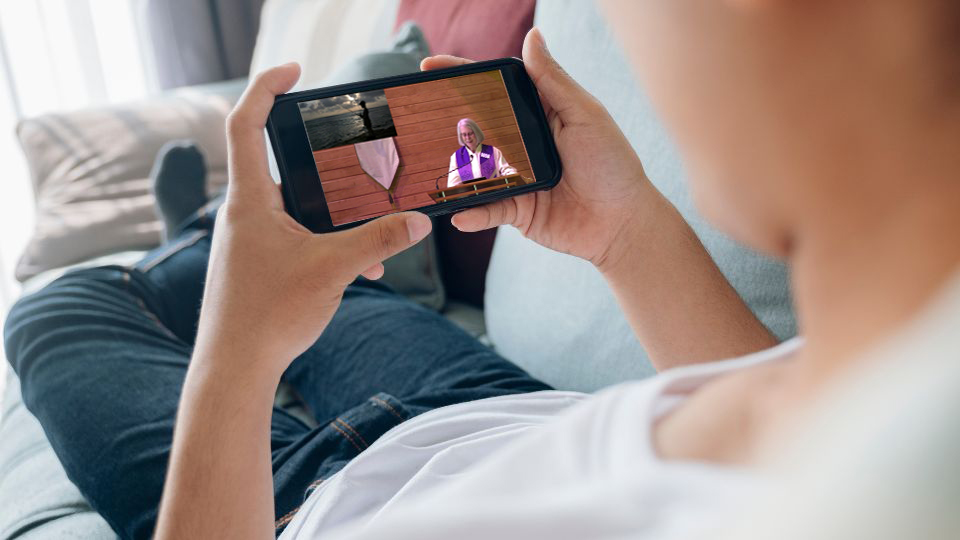 a person holding a phone watching a livestream worship service, while lounging on a couch